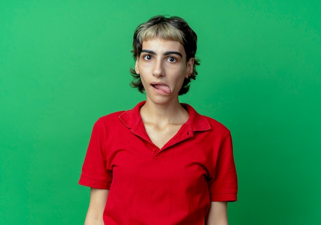 Free photo impressed young caucasian girl with pixie haircut showing tongue looking at camera isolated on green background with copy space