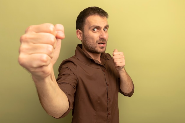 Impressed young caucasian man looking at camera doing boxing gesture isolated on olive green background with copy space