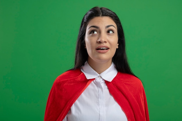 Free photo impressed young caucasian superhero girl standing right without any signs looking up isolated on green background with copy space