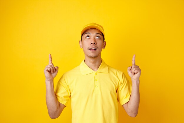 Impressed young delivery man wearing cap and uniform pointing up 