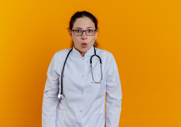 Impressed young female doctor wearing medical robe and stethoscope and glasses looking isolated