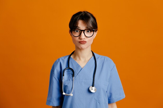 Impressed young female doctor wearing uniform fith stethoscope isolated on orange background