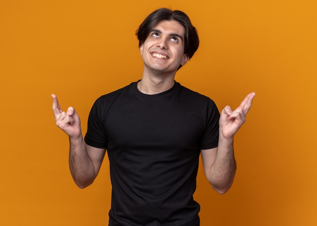 Free photo impressed young handsome guy wearing black t-shirt crossing fingers isolated on orange wall