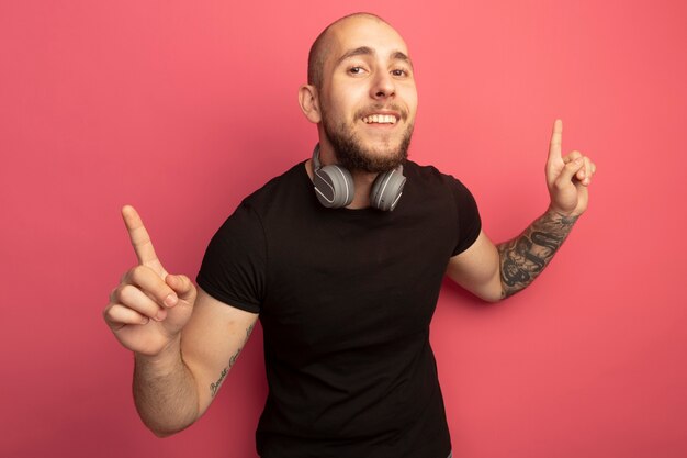 Impressed young handsome guy wearing headphones on neck points at up