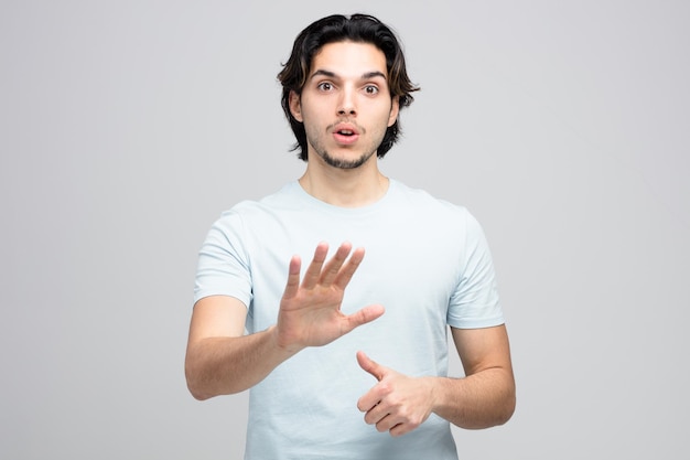 impressed young handsome man looking at camera showing thumb up and no gesture isolated on white background