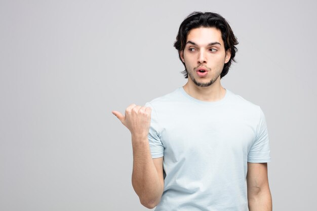 impressed young handsome man looking and pointing at side isolated on white background with copy space