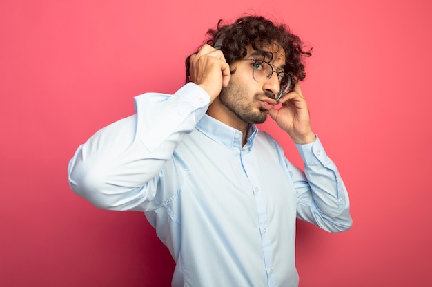 Impressed young handsome man wearing glasses and headphones looking at front touching headphones doing kiss gesture isolated on pink wall