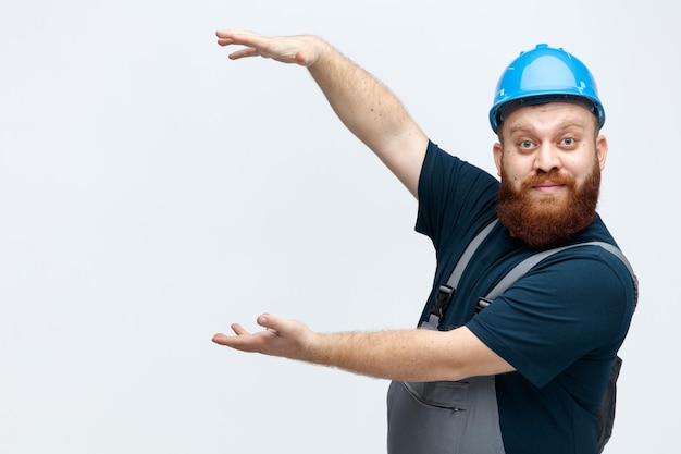 Free photo impressed young male construction worker wearing safety helmet and uniform standing in profile view looking at camera showing big size gesture isolated on white background with copy space