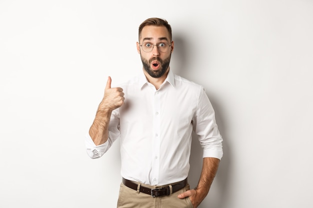 Impressed young male entrepreneur showing thumbs-up, praise something good, like and agree, white