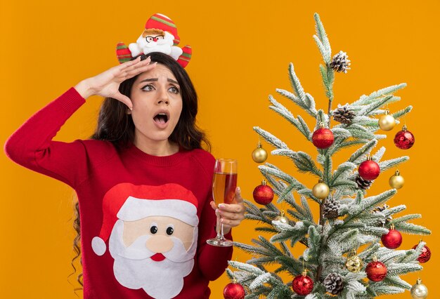 Impressed young pretty girl wearing santa claus headband and sweater 