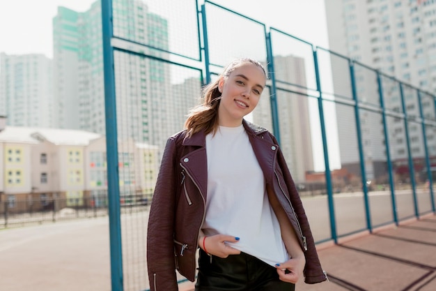 Free Photo impressive pretty girl dressed white tshirt and burgundy jacket is posing at camera with happy emotions outdoor on city recreation area background