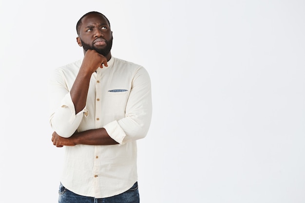 Indecisive and displeased young guy posing against the white wall