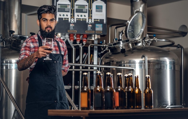 Indian bearded tattooed hipster male manufacturer tasting and presenting craft beer in the microbrewery.