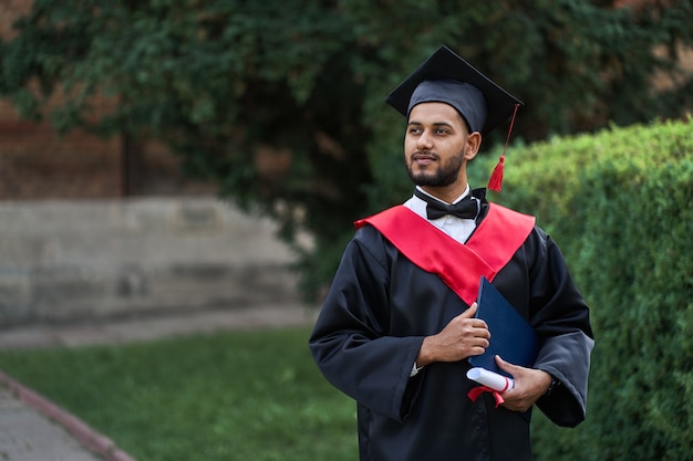 Free photo indian graduate in graduation robe with diploma in university campus copy space.