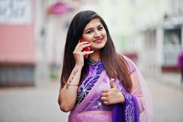 Free Photo indian hindu girl at traditional violet saree posed at street and speaking on phone shows thumb up