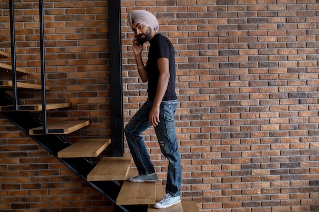 Indian man in beige turban standing on stairs and talking on the phone