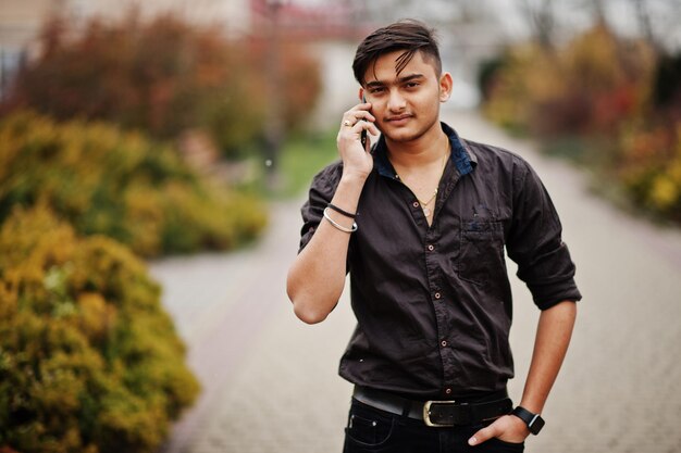 Indian man in brown shirt posed outdoor and speaking on mobile phone