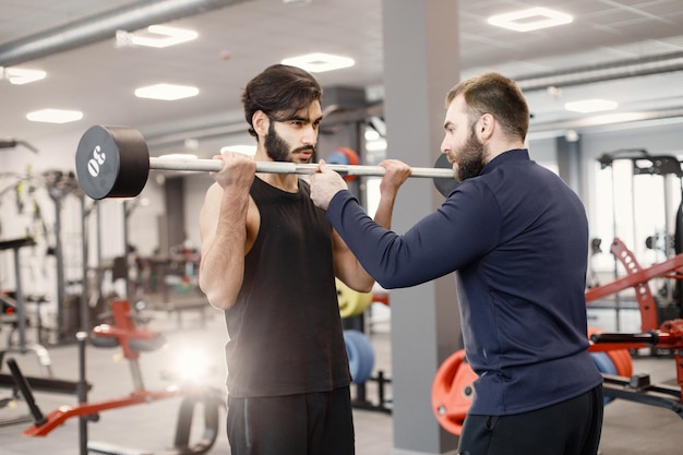 Free photo indian man doing excercisses on special equipment at gym with personal trainer