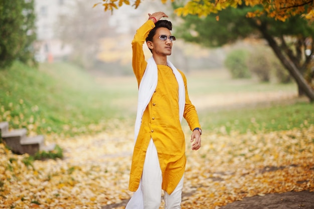 Free photo indian stylish man in yellow traditional clothes with white scarf sunglasses posed outdoor against autumn leaves tree