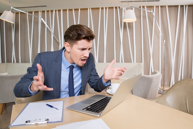 Indignant Businessman Working on Laptop in Cafe