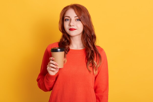 Indignant woman with calm facial expression, has coffee break, holds paper cup, 