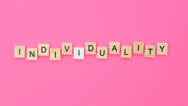 Individuality lettering made with wooden cubes on pink background