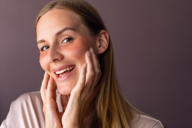 Indoor close up portrait of blonde woman make skin care routime, use eye patches, spa at home concept. Anti age.