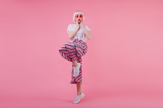 Free Photo indoor photo of amazed pretty girl in pink periwig funny posing on pink wall.  refined caucasian lady in fashionable attire dancing and expressing surprised emotions