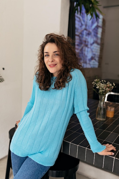 Free Photo indoor photo of beautiful girl with curls in tender blue pullover is smiling at camera and resting in cafe