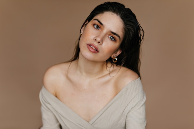 Indoor photo of elegant girl in golden accessories. Beautiful lady in earrings posing with interest.