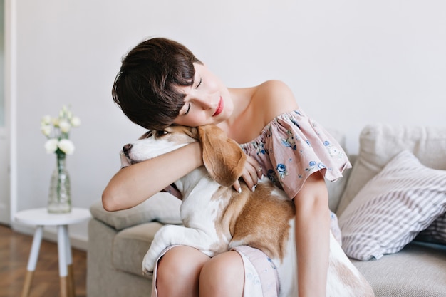 Free Photo indoor portrait of dreamy brown-haired girl in vintage attire embracing beagle dog with eyes closed