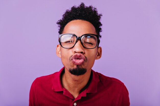 Indoor portrait of funny african man posing with kissing face expression. Close-up photo of carefree brunette boy fooling around.