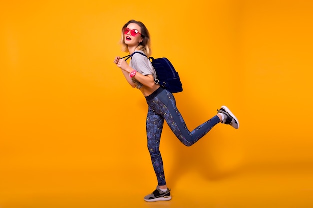 Free Photo indoor portrait of laughing girl playing with muscles on yellow background. shapely young woman in leggings and gray t-shirt holding bottle of water and doing sports.