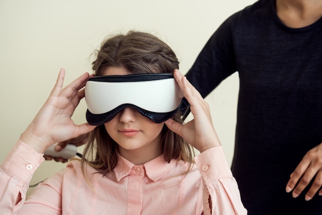 Free photo indoor portrait of relaxed and confident caucasian woman on appointment with optometrist sitting in her office while testing sight with digital vision screener, wearing it on eyes