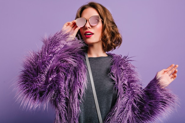 Indoor portrait of stylish european female model in glasses posing on purple background