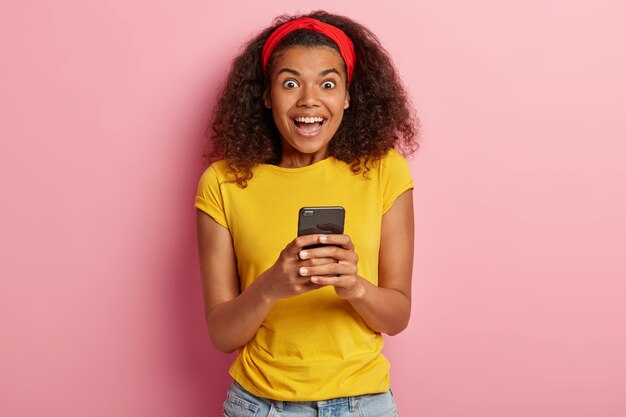 Indoor shot of amused teenage girl with curly hair posing in yellow tshirt