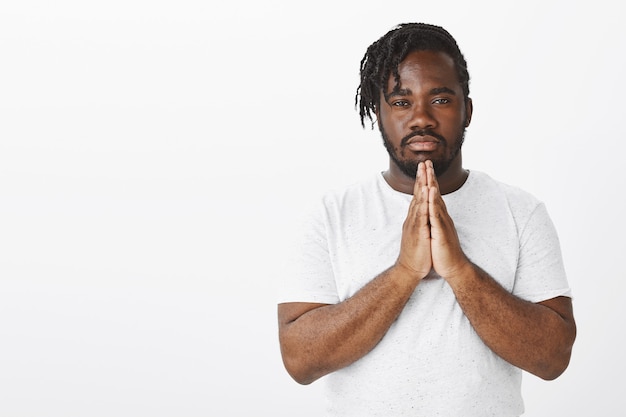 Indoor shot of calm guy with braids posing against the white wall