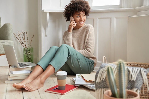 Indoor shot of cheerful satisfied dark skinned businesswoman or entrepreneur works on creating new plan