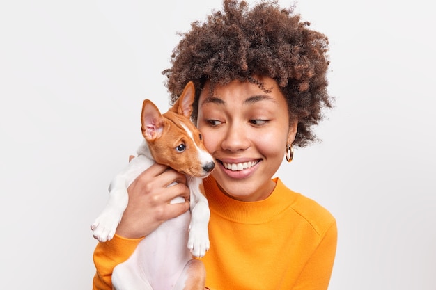 Indoor shot of friendly woman and dog take pleasure while playing together have good relationships enjoy good moment. Positive female pet owner holds small puppy. Animals and people concept.