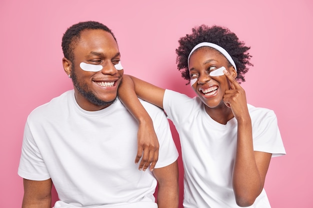 Indoor shot of happy carefree black woman and man looks with smile at each other apply beauty patches 