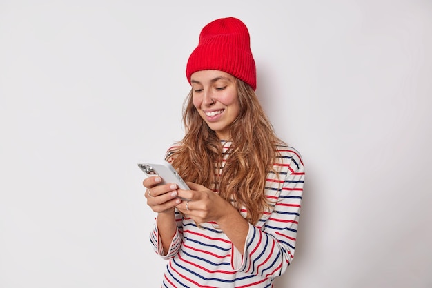 Free Photo indoor shot of happy millennial girl sends text messages via smartphone uses application has piercing in nose dressed in casual clothes isolated on white. modern technologies concept