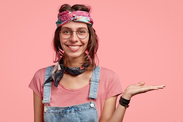 Indoor shot of smiling hippy wears stylish headband and spectacles holds copy space