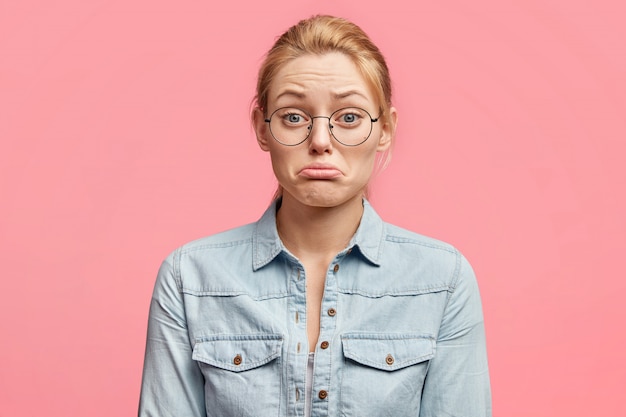 Free photo indoor shot of sorrowful woman with upset expression, has troubles with husband`s relationship, curves lower lip in dissatisfaction, wears fashionable clothing