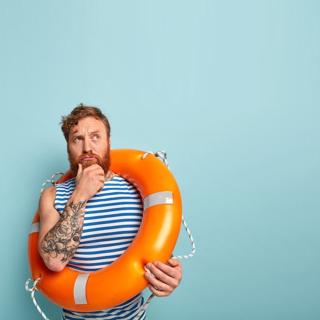 Free photo indoor shot of thoughtful inexperienced male swimmer holds chin, focused upwards