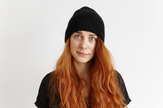 Indoor studio shot of cute redhead hipster girl wearing t-shirt and hat having indignant and blaming look