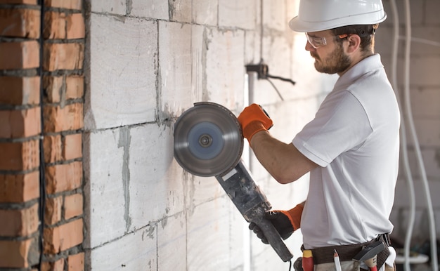 Free photo the industrial builder works with a professional angle grinder to cut bricks and build interior walls. electrician.