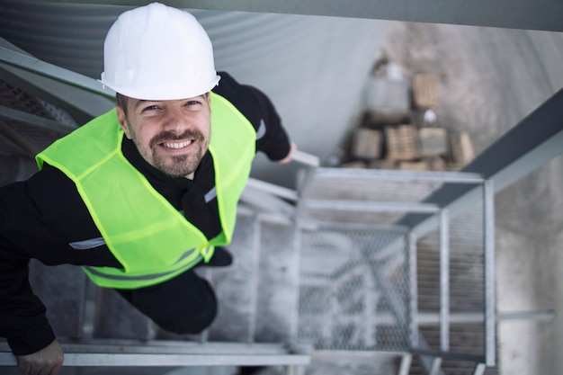 Industrial factory worker in protective equipment standing on metal staircase of production plant