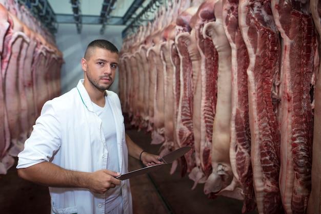 Industrial food worker handling fresh raw meat in slaughterhouse and preparing meat for the market