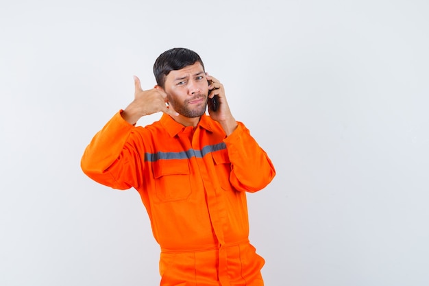 Industrial man talking on mobile phone with phone gesture in uniform front view.