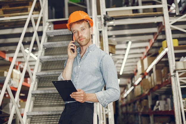 Industrial worker indoors in factory. Businessman with orange hard hat. Man in a blue shirt.